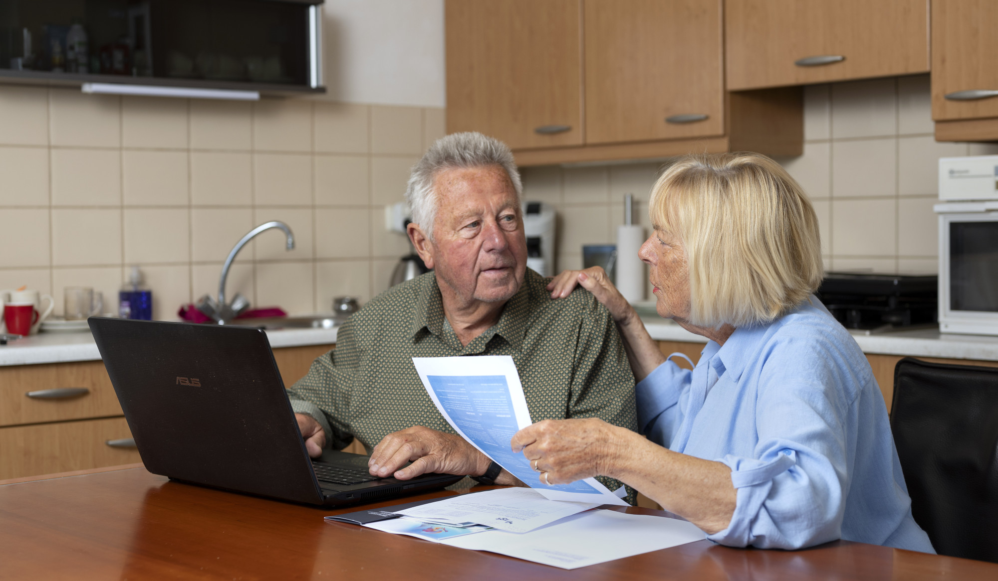Twee personen aan keukentafel met laptop en document